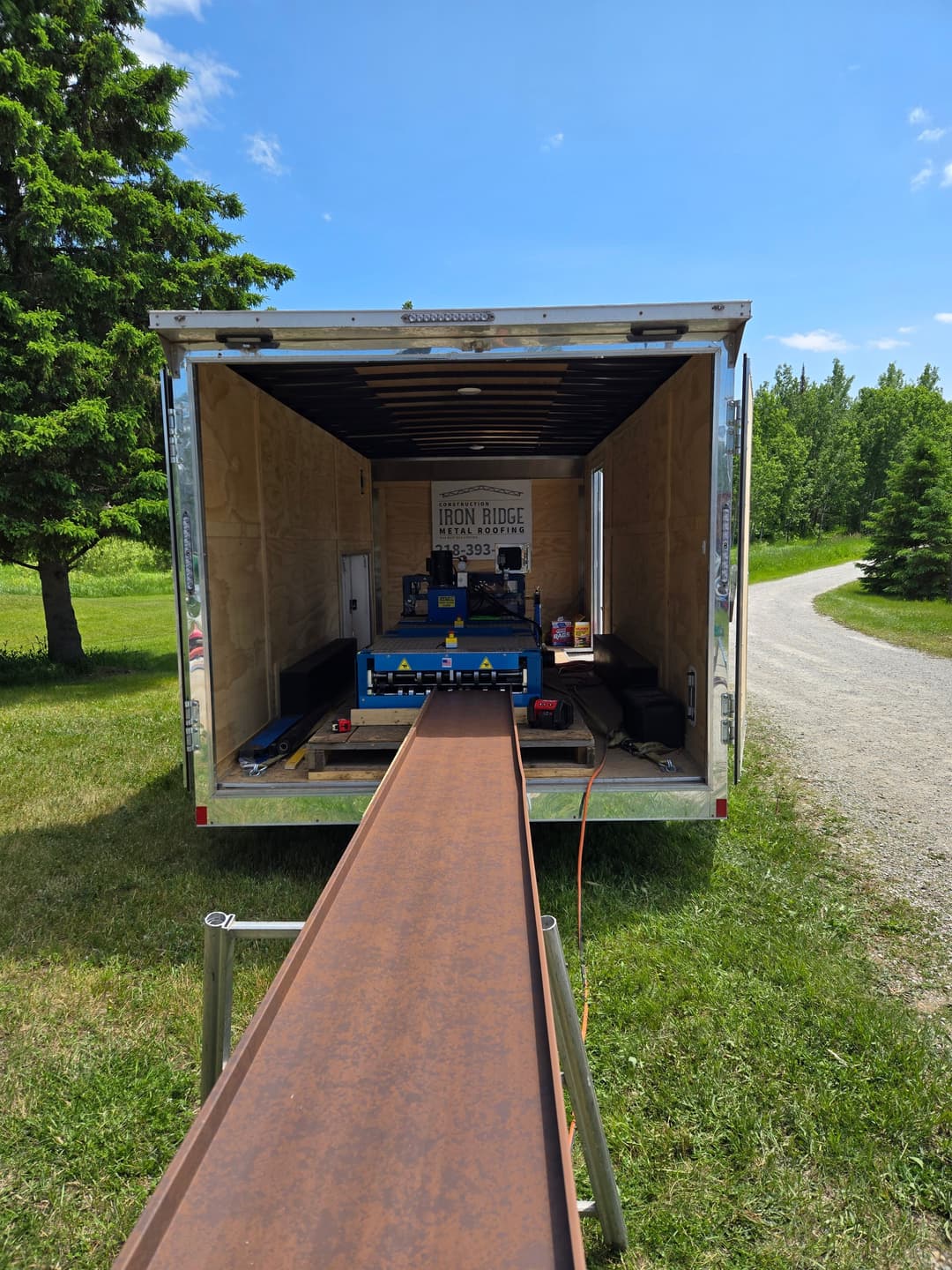 View of a trailer interior with a conveyor belt, tools, and green landscape outside.
